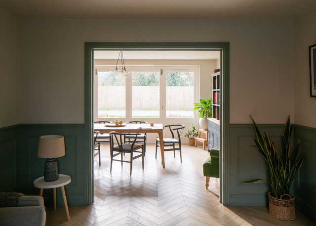 View through doorway to dining room with wooden table, black chairs, and large windows overlooking garden.