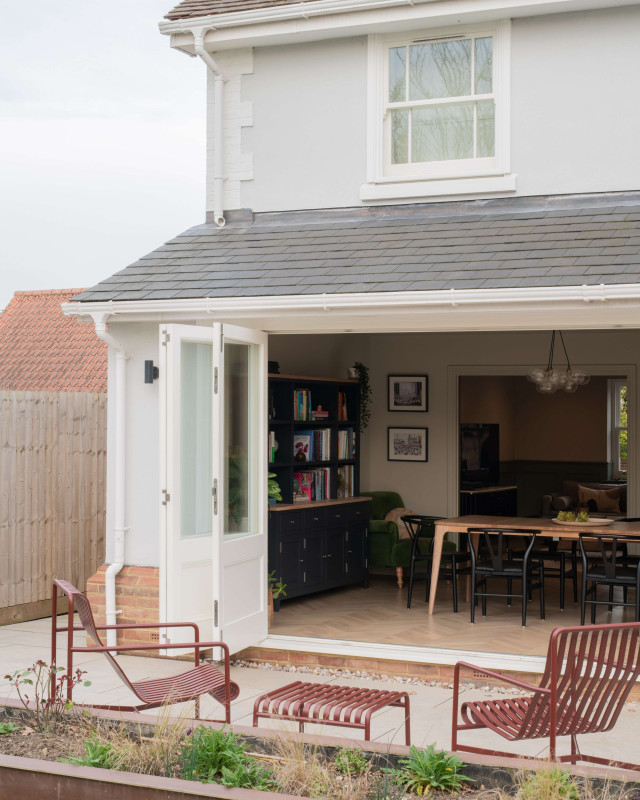 Exterior view of house with open French doors leading to dining area, with patio seating in the foreground.