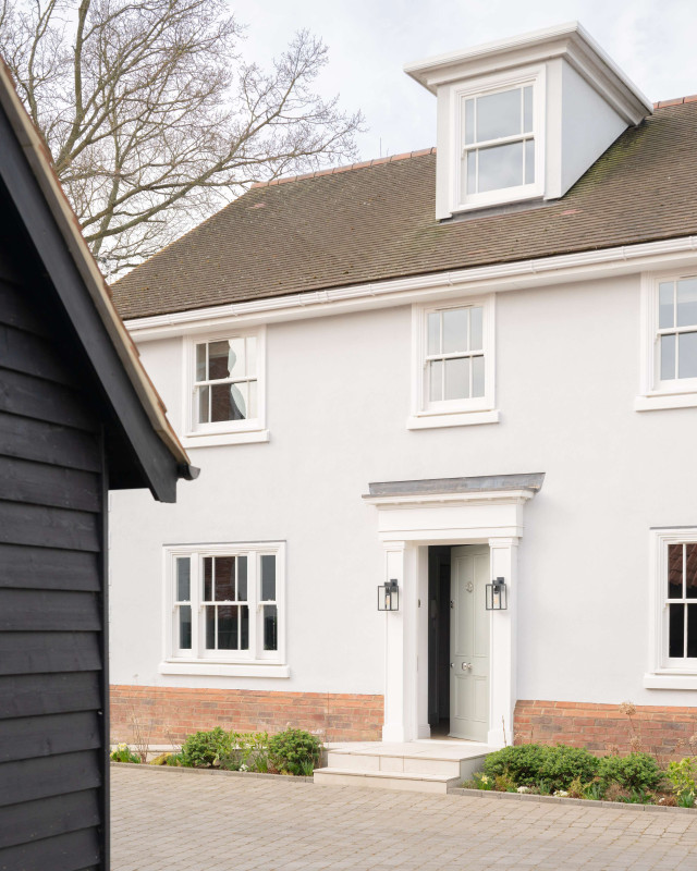 White three-storey house with dormer window, brick detailing, and central front door with lantern lights.