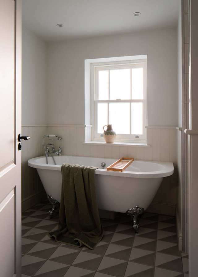 Bathroom with freestanding clawfoot bathtub, patterned tiled floor, and window above.