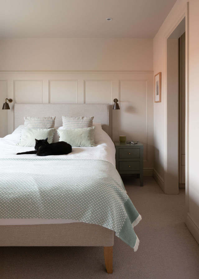 Bedroom with upholstered bed, soft green blanket, wall panelling, and bedside table.