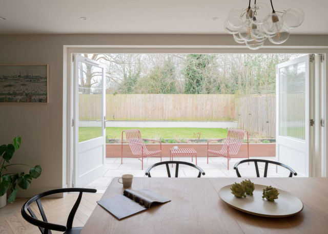 Dining room with French doors opening onto patio seating and garden view.