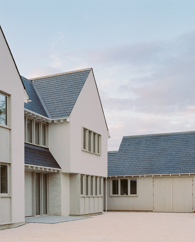 Contemporary house with steep pitched slate roofs, pale rendered walls, and timber-clad sections surrounding a clean, open courtyard.